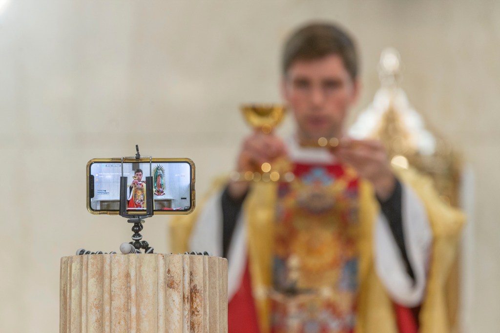 The Rev. Matthew Wheeler is seen on an iPhone screen live-streaming the celebration of the the Mass of the Lord's Supper at St. Anthony Parish in San Gabriel, Calif., Thursday, April 9, 2020. With no public Mass due to the coronavirus pandemic, the church live-streams its services. Photo by AP Damian Dovarganes, AP Photo