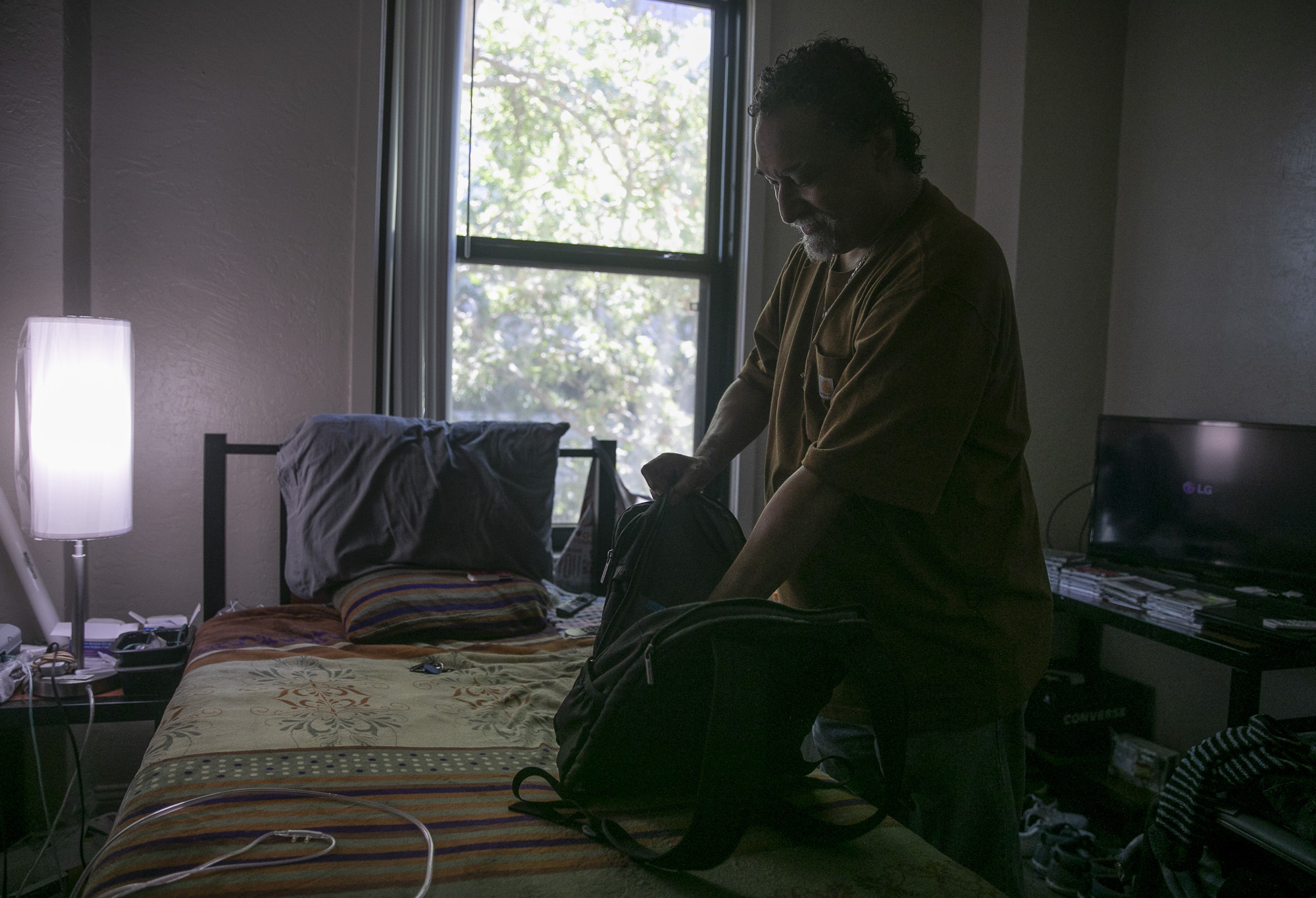 Salvador Bradford tidies his studio at Hotel Berry. Bradford has been living in the one-room unit for 8 months and spends most of his time watching movies and keeping his room organized. Photo by Anne Wernikoff for CalMatters