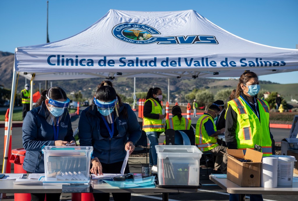 Two Clinica de Salud del Valle de Salinas employees look through a binder during a COVID-19 vaccine distribution event in Salinas on Feb. 25, 2021. Clinica de Salud del Valle de Salinas partnered with the Grower-Shipper Association to begin vaccinating farmworkers in February when Monterey County was still prioritizing residents over 65. Photo by David Rodriguez, The Salinas Californian