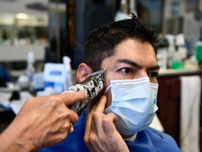 Carlos Hernandez holds his mask while getting a haircut from Sarah Cordiey at Spiros Barber Shop in Long Beach, on June 9, 2021. "During the pandemic, I got depression and anxiety," said Hernandez, who saw his family last week for the first time in more than a year. "But then when I got [fully] vaccinated I felt a lot better." Pablo Unzueta for CalMatters