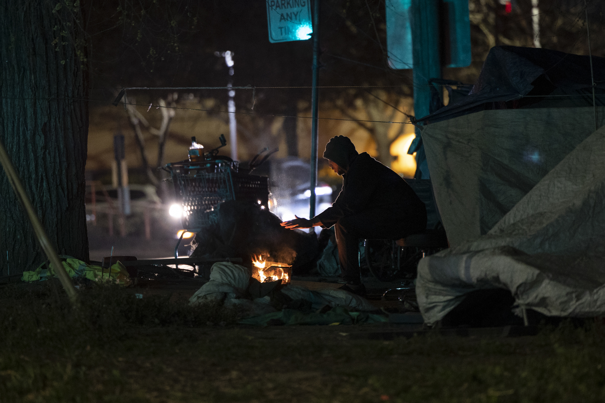 Muhammad, who declined to provide his last name, warms his hand at a fire near his tent in Sacramento. Photo by Miguel Gutierrez Jr., CalMatters