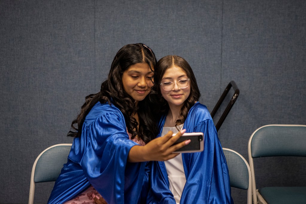 Lorena Hernandez (left) and her friend Yoselyn Cuellar (right) take a selfie together as they get ready for their 8th-grade graduation ceremony at Buttonwillow Union School's music room on May 26, 2022. Photo by Larry Valenzuela for CalMatters