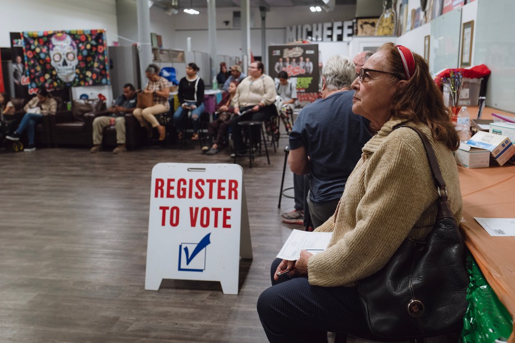 Rosalinda Avitia, 73, listens to organizers as they review voter registration information in Tulare on Nov. 1, 2023. Photo by Zaydee Sanchez for CalMatters