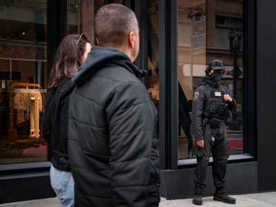 A security guard stands by the front entrance of a luxury retail storefront in downtown San Francisco on April 15, 2024. Retail theft has plagued the area, and numerous storefronts sit vacant. Photo by Loren Elliott for CalMatters
