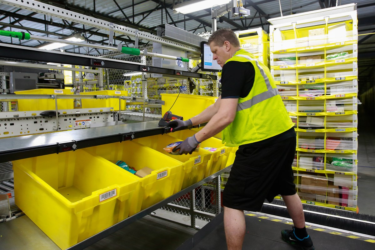 A worker wearing a yellow vest scans items and places them into yellow bins as they move through the Amazon Fulfillment Center in Sacramento in 2018. Photo by Rich Pedroncelli, AP File