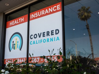 A red, white, dark blue and light blue Covered California health insurance sign on a large window in Chula Vista.