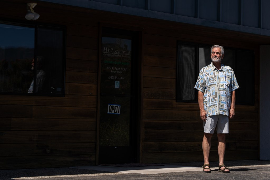 John Reed, wearing a blue and teal pattern shirt with khaki shorts, outside of the MVP Commercial building, with a wood and gray exterior, in Oakhurst, on Aug. 11, 2024. Photo by Tracy Barbutes for CalMatters