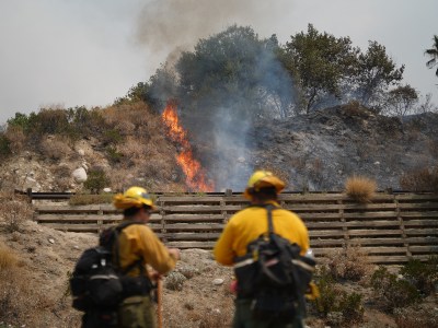 Two firefighters stand overlooking a nearby a small fire on a mountain.