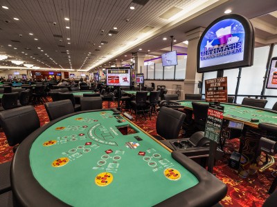 A wide view of green tables where people play texas hold em at a casino.