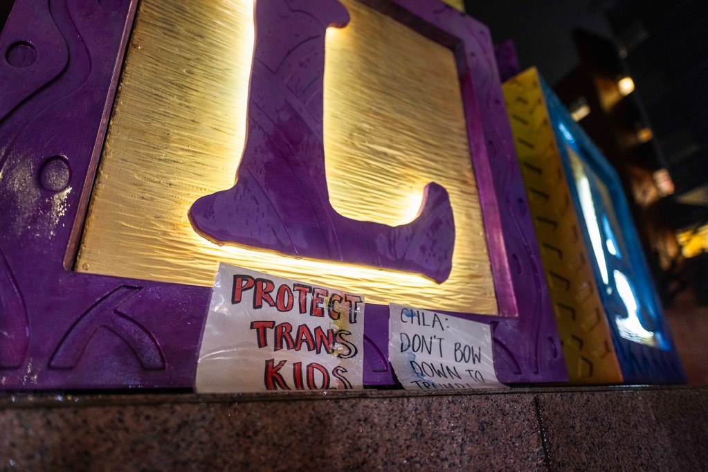 Paper signs are placed at the foot of a giant letter block sculpture outside a hospital during a recent evening. One sign reads "Protect Trans Kids" and the other reads "CHLA: Don't bow down to Trump."